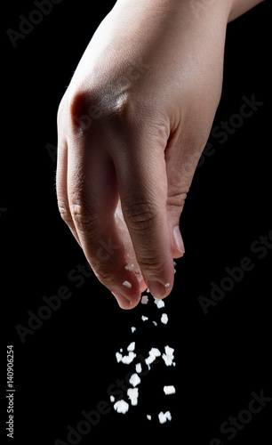 Hand sprinkling salt over black background.