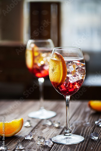 refreshing red cocktails with orange isolated on a wooden background with oranges and ice against big window