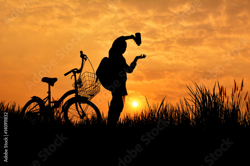 Silhouette of girl with bicycle on grass field at the sky sunset, color of vintage tone and soft focus concept journey