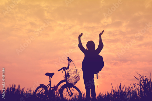 Silhouette of girl with bicycle on grass field at the sky sunset, color of vintage tone and soft focus concept journey