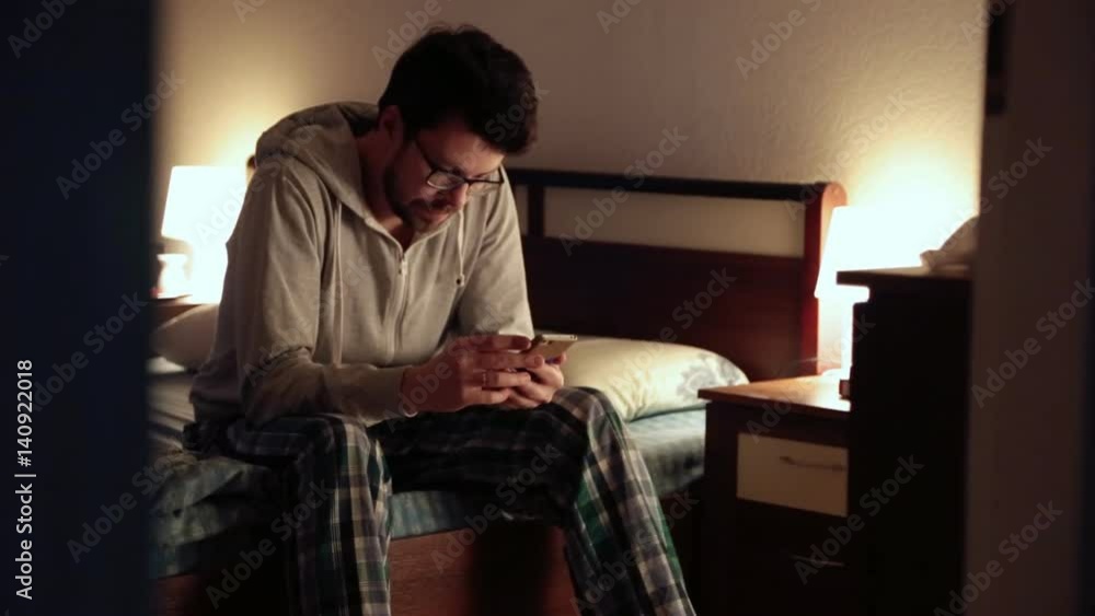 the guy sitting on the bed in the bedroom and looks at the phone the guy sitting on the bed in the bedroom and looks at the phone
