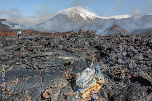 The active lava flow from a new crater on the slope of a volcano Tolbachik and a group of tourists, which boosts his - Kamchatka, Russia photo
