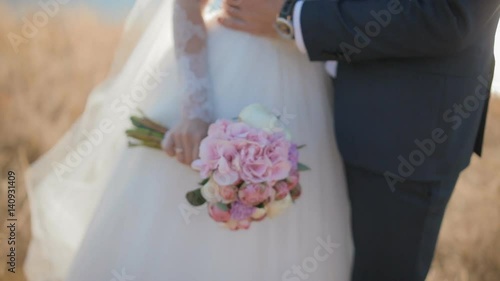 Bride and groom posing to photographer near the river. Young people embrace each other gently.