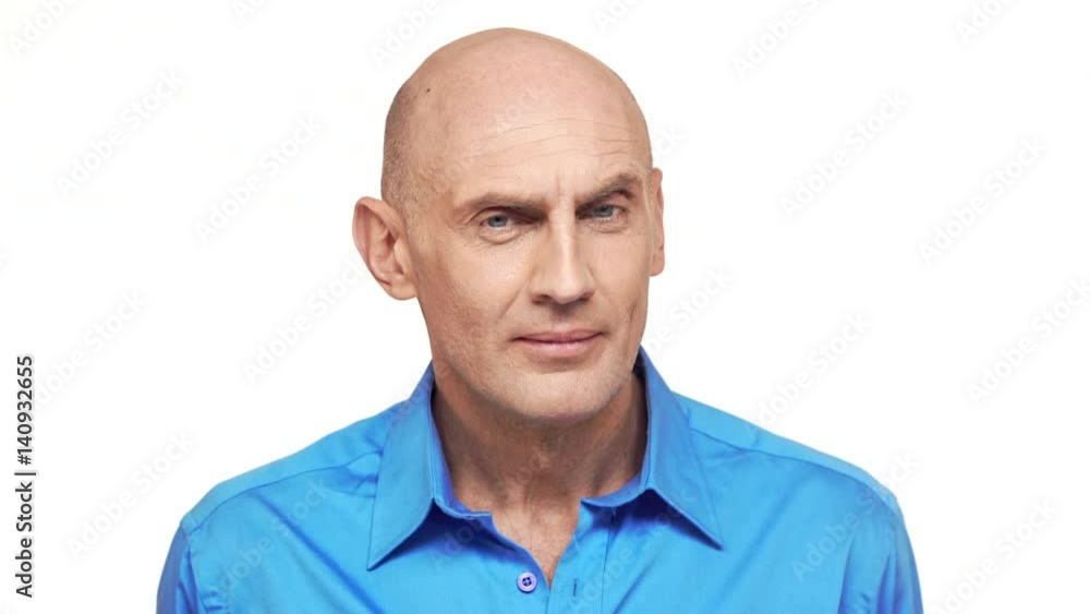 Bold Caucasian middle-aged male in blue shirt seriously peering at camera standing on white background Bold Caucasian middle-aged male in blue shirt seriously peering at camera standing on white background