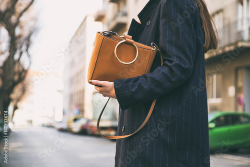 detail of a fashionable woman wearing a navy blue oversized coat and a brown trendy handbag. perfect spring fashion outfit.


