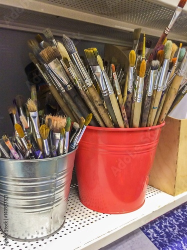 Art Studio. Many dirty brushes in red and silver buckets.