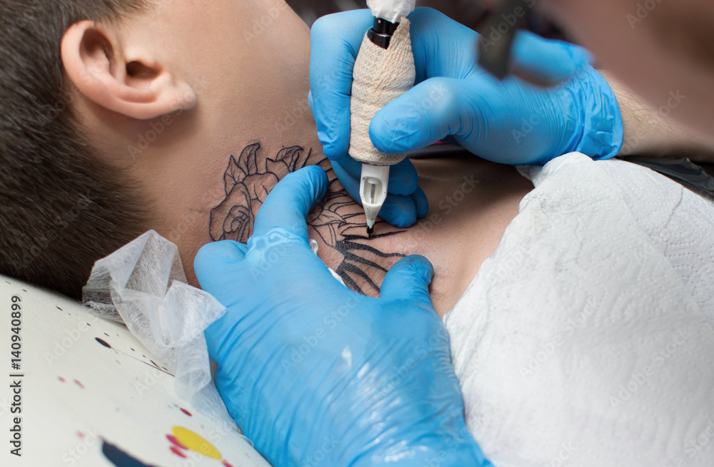 The tattoo artist makes a tattoo on the client's neck in the tattoo ...