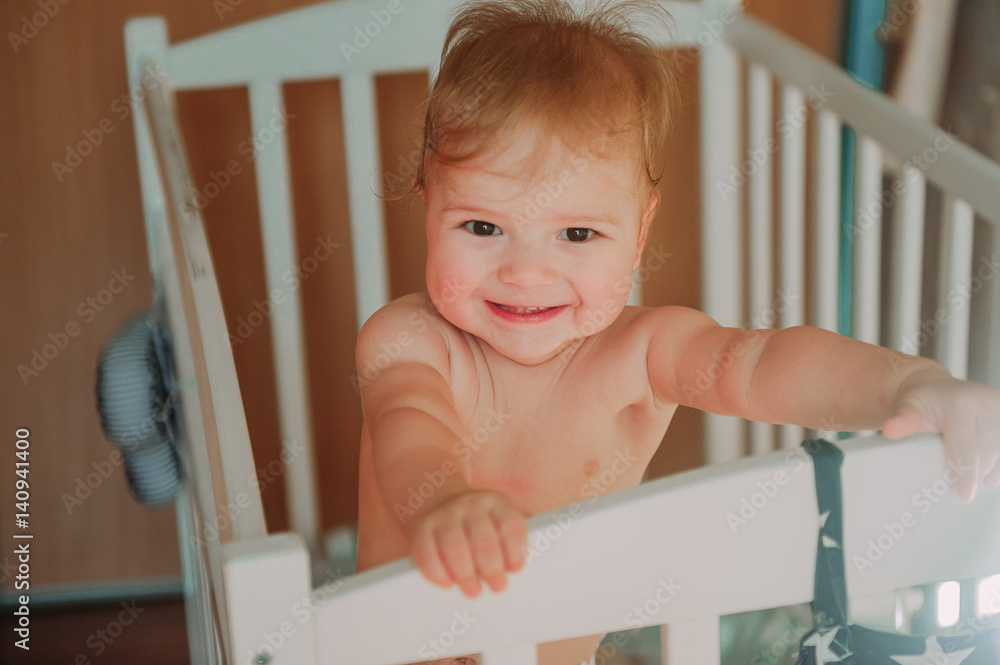 Happy cute baby boy smiling with teeth and sitting in the crib, just woke up