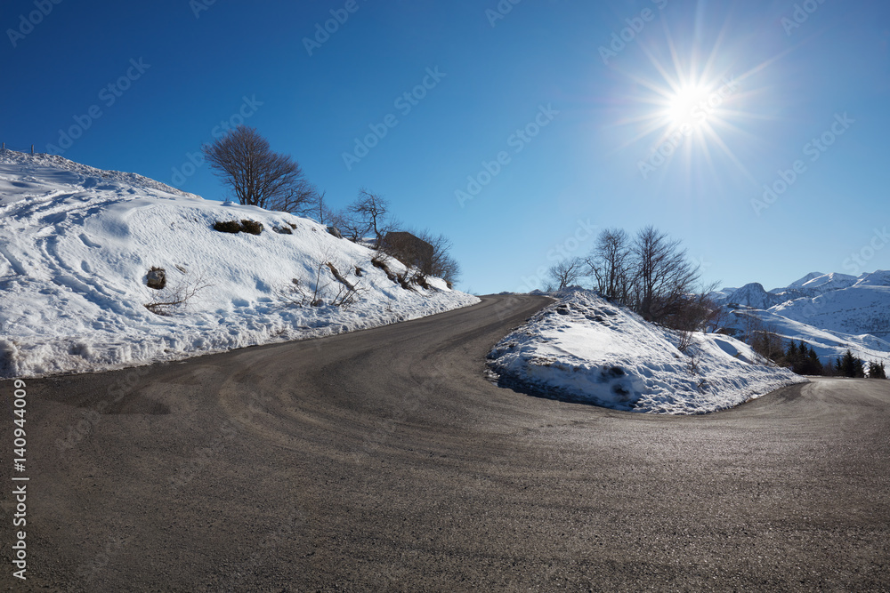 Empty mountain road curve on Alps with snow on sides, blue sky in a sunny day
