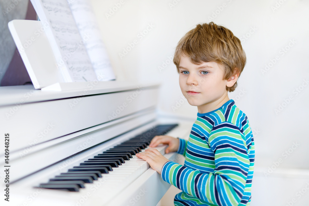 Fototapeta Beautiful little kid boy playing piano in living room or music school