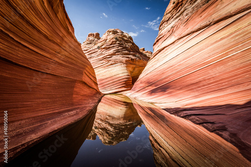 Arizona - Utah border, a stunning rock formation known as The Wave in the rocky desert, reflecting on a rare water puddle photo