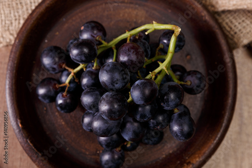 Dark grapes bunch. Ripe grape fruit on rustic plate. On wooden background.