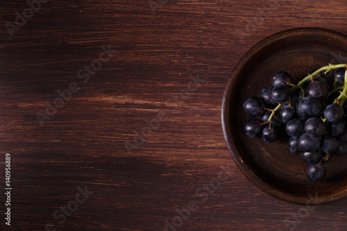 Dark grapes bunch. Ripe grape fruit on rustic plate. On wooden background.