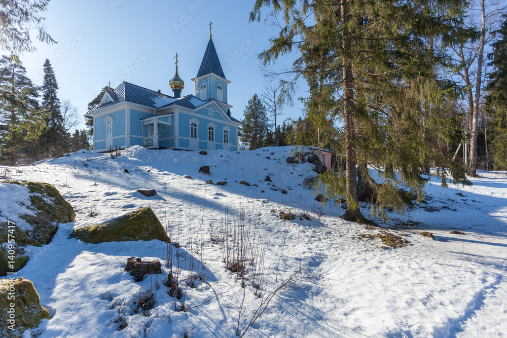 Blue church surrounded by winter forest on a sunny day