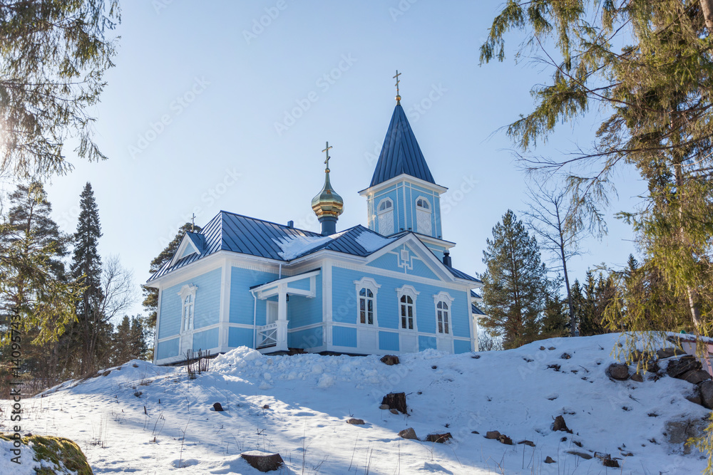 Blue church surrounded by winter forest on a sunny day