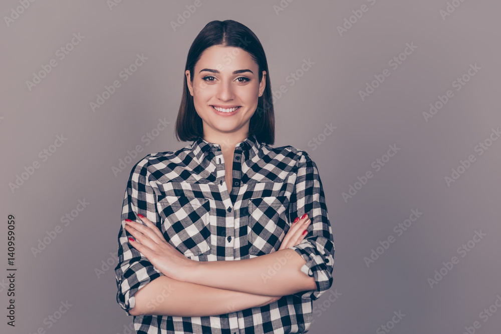 A horizontal photo of a young smiling happy lady with crossed hands standing in front of gray background