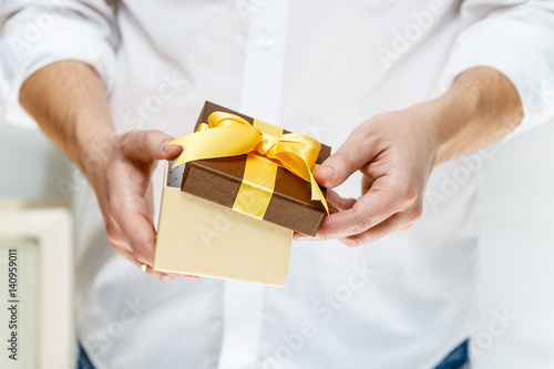 Male hands holding a gift box. Opened present wrapped with ribbon and bow. Christmas or birthday package. Man in white shirt.