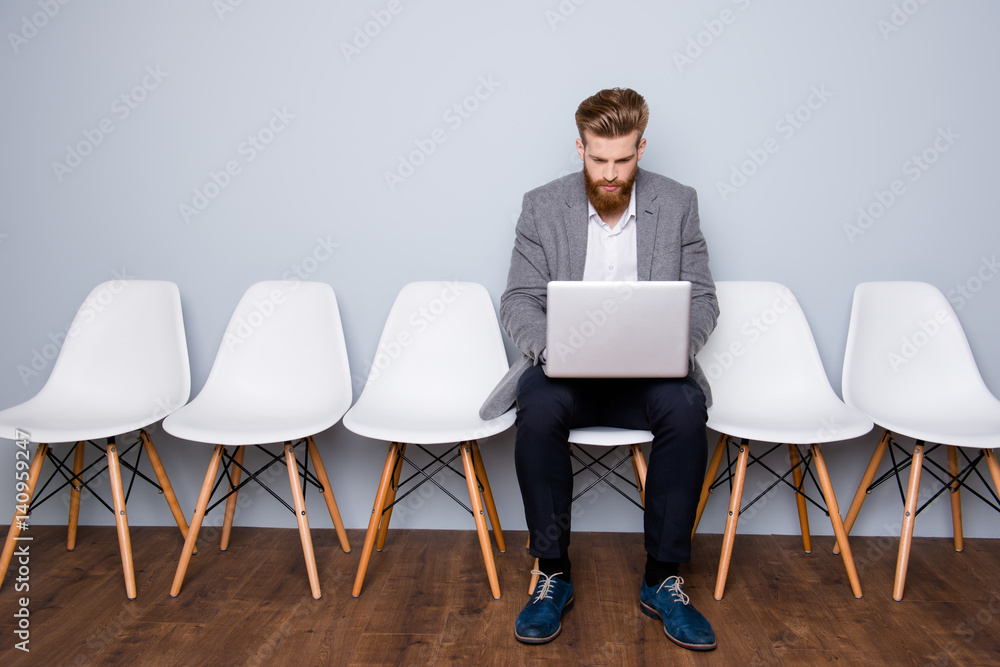 Fototapeta premium Portrait of young successful businessman sitting on a chair and working with laptop