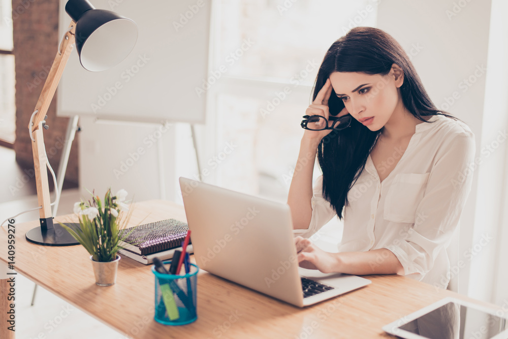 Portrait of serious beautiful concentrated young businesswoman sitting at the desktop in office and work with laptop Portrait of serious beautiful concentrated young businesswoman sitting at the desktop in office and work with laptop