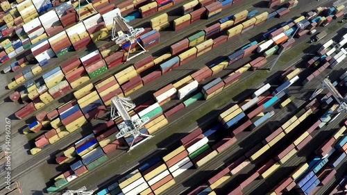 Aerial top down view flying over container terminal showing many intermodal containers used for freight transport shipping goods stacked up on each other different colors cranes moving in between 4k