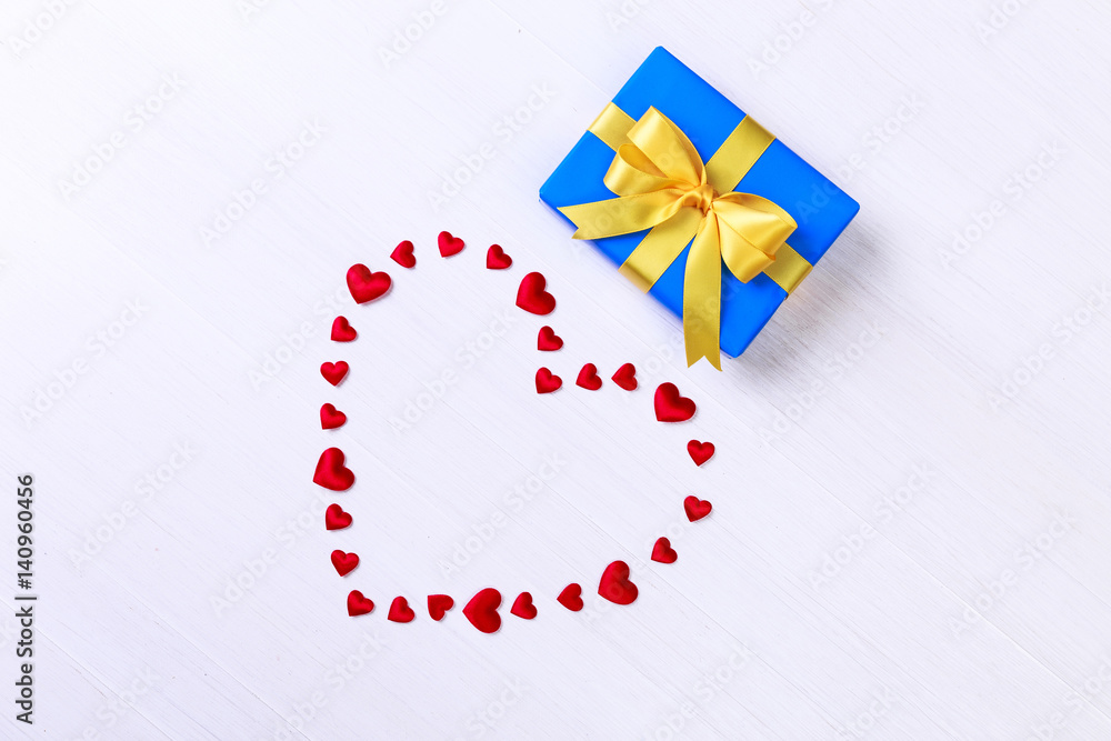Gift box with red heart. Present wrapped with yellow ribbon. Christmas or birthday blue package. On white wooden table. Gift box with red heart. Present wrapped with yellow ribbon. Christmas or birthday blue package. On white wooden table.