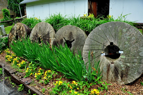 Lancaster, Pennsylvania - June 5, 2015:  Row of round millstones decorates a garden with Iris, Pansies, and Daylilies at the historic 1719 Hans Herr House