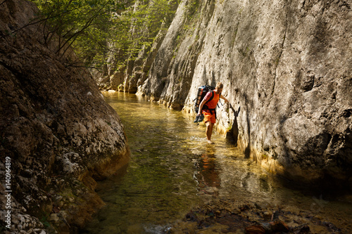 Man walks through the narrow mountain canyon river with his shoes in his hand