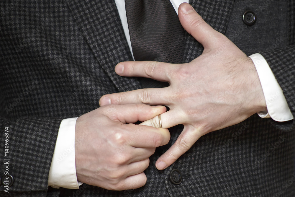 a man in jacket struggling to remove wedding ring from his finger