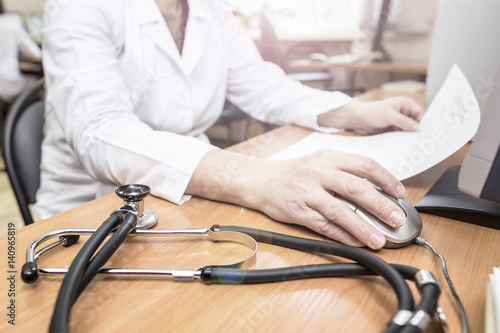 a doctor at the computer analyzes the data of the patient medical research, on the table next to stethoscope