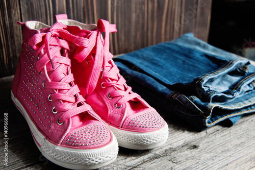 a pink shiny shoes and blue jeans for girls on a wooden background