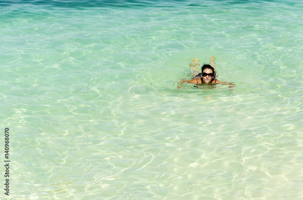 Woman with glassses floating and relaxing in turquoise waters at colorful tropical beach