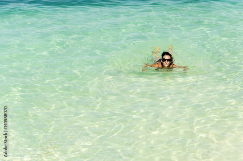 Woman with glassses floating and relaxing in turquoise waters at colorful tropical beach