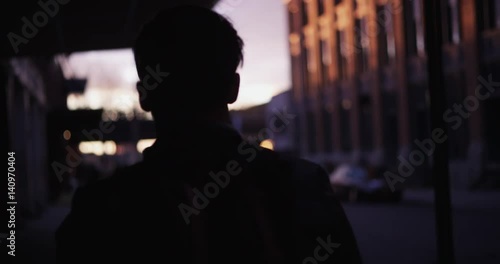 Young man walks down NYC street, sunset