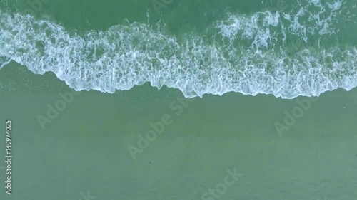 Top view foamy waves wash sandy beach aerial shot, shooting from helicopter, Camera moving from right to left