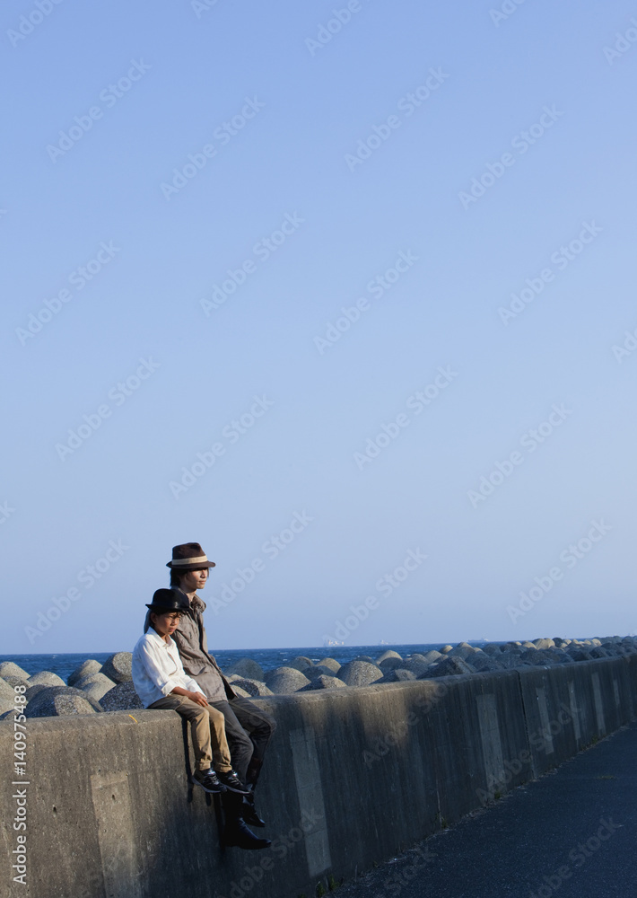Father and son sitting on breakwater