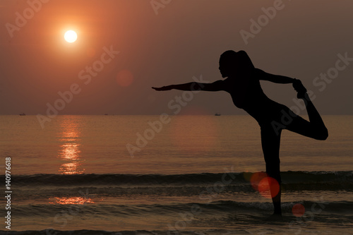 Silhouette of woman making yoga on the beach with sunset background