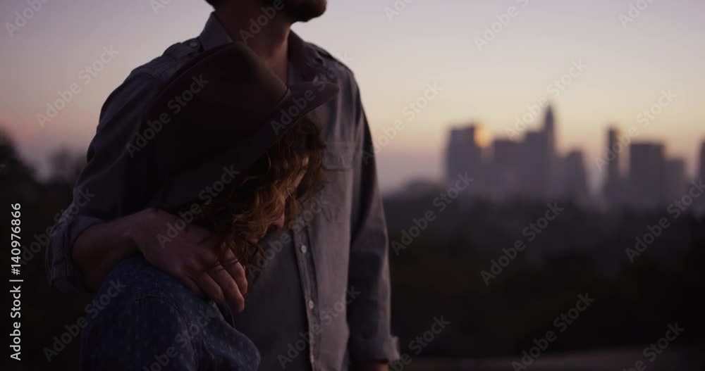 Man lays arm around woman, slow motion sunset, LA cityscape in background Man lays arm around woman, slow motion sunset, LA cityscape in background