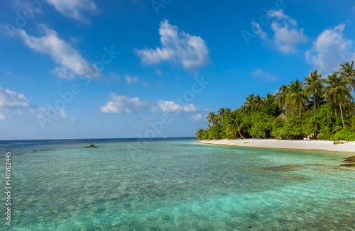 Landscape of a tropical blue turquoise crystal clear ocean water and sandy beach in Maldives island. Blue cloudy sky in the background.