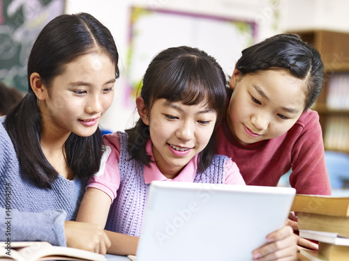 asian elementary schoolgirls using tablet during break in classroom