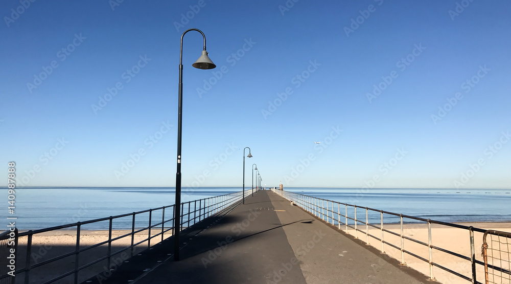 Lamp posts on empty pier stretching out into sea on clear summer day