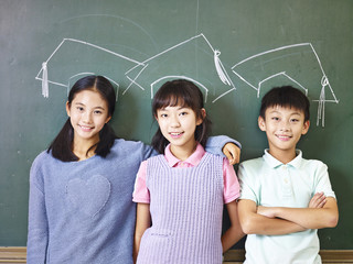 asian elementary school students standing underneath chalk-drawn doctoral hats