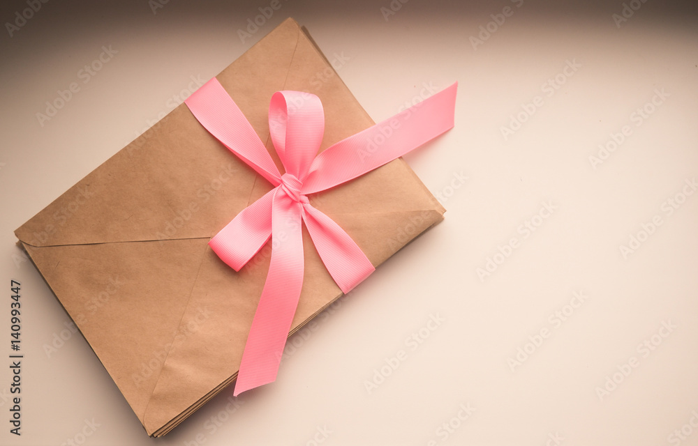 Kraft envelope tied with a pink ribbon on a wooden background. Homemade gift envelope with pink ribbon Kraft envelope tied with a pink ribbon on a wooden background. Homemade gift envelope with pink ribbon