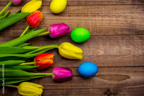 Easter eggs and fresh spring tulips on weathered wooden background