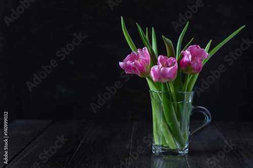 Fresh pink tulip flowers bouquet in a glass jar on dark background