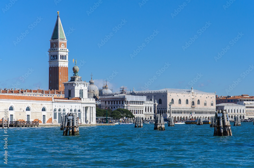 Venice: St. Mark square with Campanile viewed from Grand Canal, with old wooden navigation markers in the foreground