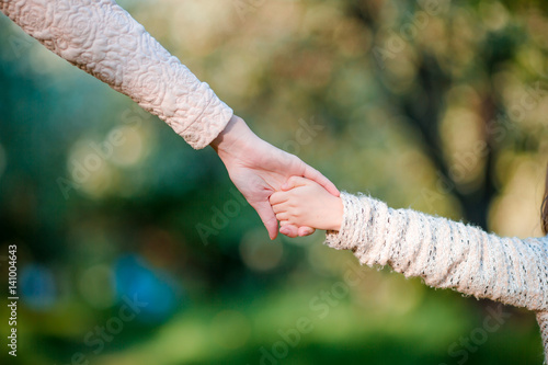 Young parent holds the hand of a small kid