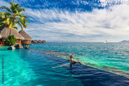 Woman in the infinity pool in exotic island resort with bunalows over water