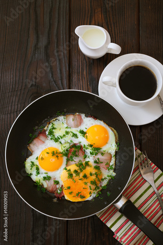 Fried eggs with bacon in a frying pan and coffee on a wooden table