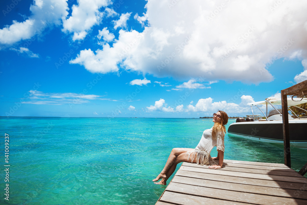 Woman enjoyong sun, sitting on pier with legs in water Woman enjoyong sun, sitting on pier with legs in water