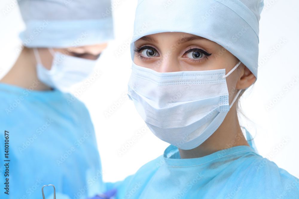 Close up of surgeon woman looking at camera while colleagues performing in background in operation room, isolated. Surgery and medicine concept Close up of surgeon woman looking at camera while colleagues performing in background in operation room, isolated. Surgery and medicine concept